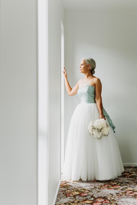 Bride holding bouquet by window in wedding dress.